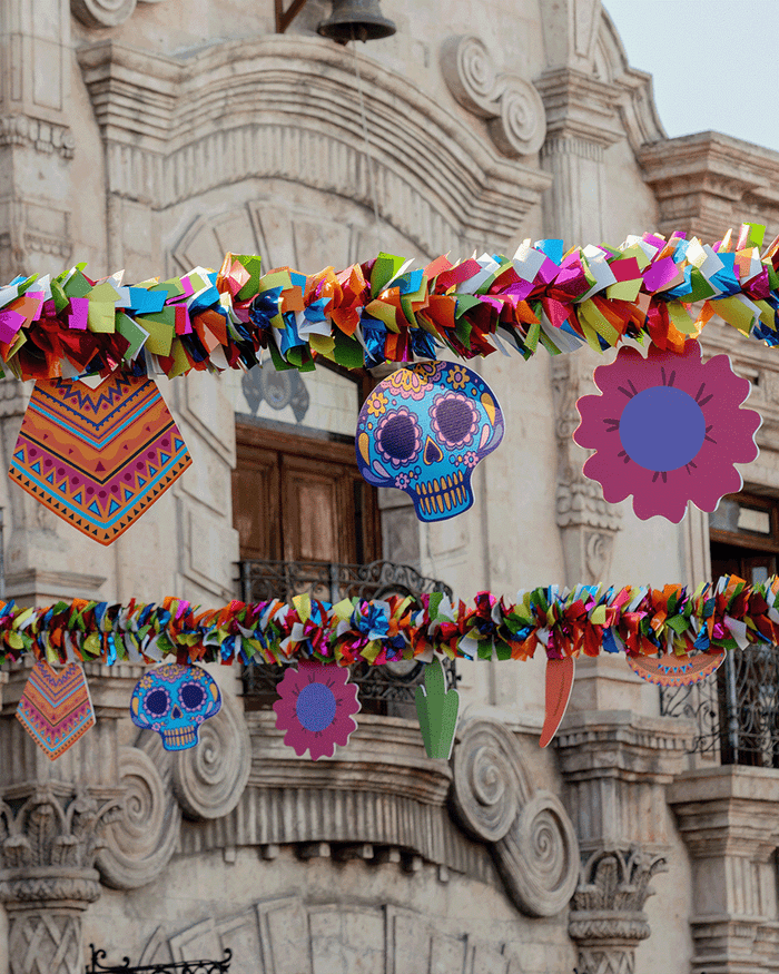 Custom graphics for Cinco de Mayo including a blue and purple and yellow sugar skull, an orange and pink and blue poncho, a cactus, a chili pepper, a flower, and a sombrero all hanging from rainbow garland.