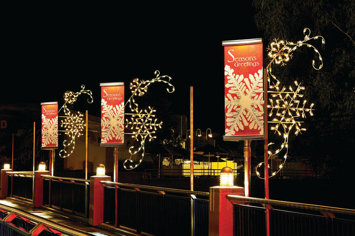 Three holiday pole banners with a snowflake and white text that says Season's Greetings on a red background. Each banner is surrounded by a lit snowflake decoration.