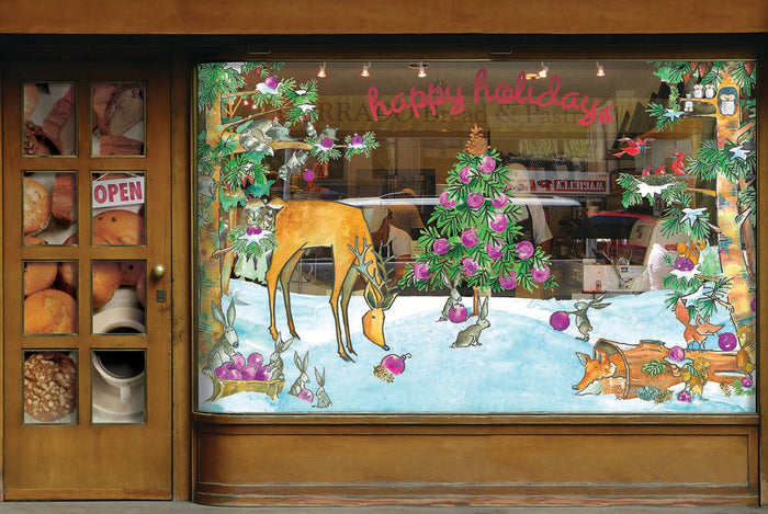 A window display decorated for Christmas with custom graphic stickers of reindeer eating berries on a blanket of snow surrounded by Christmas trees.