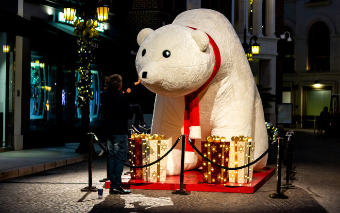 A giant polar bear Christmas inflatable surrounded by illuminated red and white gift box props.
