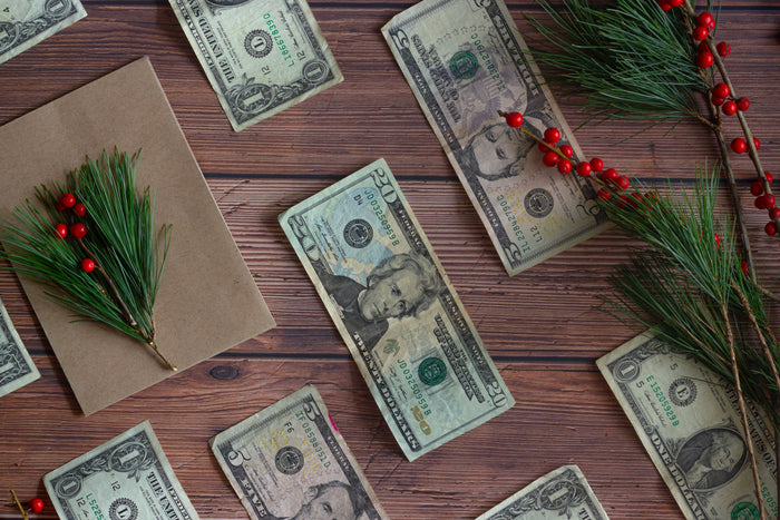 Flat lay of a wooden table covered in neatly placed 1, 5, and 20 dollar bills with holiday foliage and berries scattered throughout.