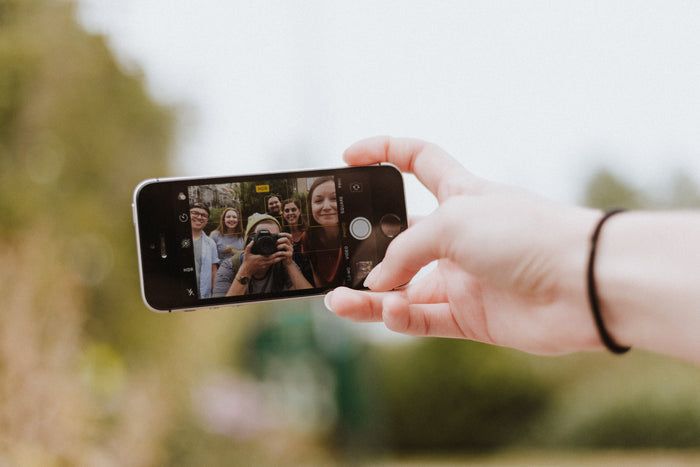 A hand holding a phone with the screen showing a group of people taking a selfie.