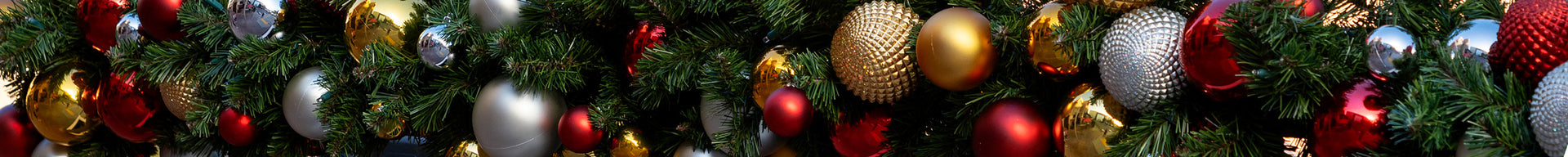Close-up of artificial garland heavily decorated with gold, red, and silver ornaments of varying sizes and textures.