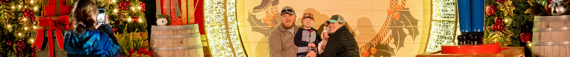 A family of four poses in front of a custom backdrop while a woman takes a photo with her phone.