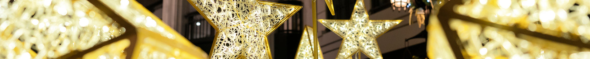 Cross section of small illuminated gold star decorations at an outdoor shopping center.