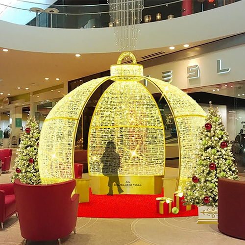 A large, illuminated Christmas ornament shaped like a ball, made of gold wire with a handle at the top. The ornament is decorated with festive lights, making it a popular decoration for homes and businesses during the holiday season.