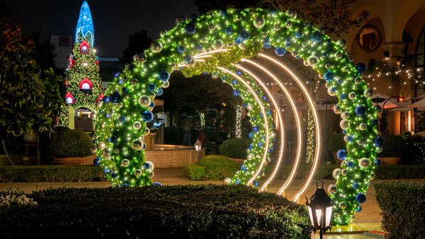 Illuminated Christmas tree tunnel entrance with warm white 
lights and spherical ornament decorations creating immersive 
holiday walkthrough display