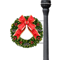 A festive Christmas wreath with a large red bow, gold trim, green pine needles, small red ornaments, and warm white string lights, shown hanging against a black background next to a dark decorative pole.