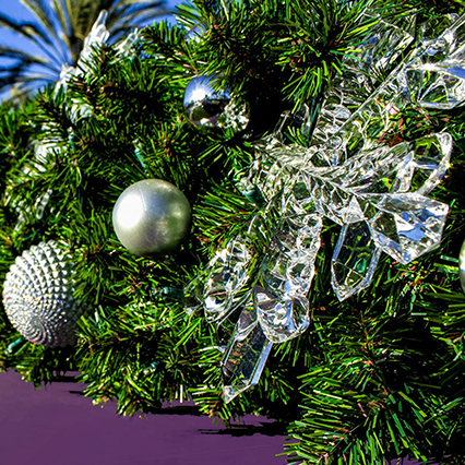 A close-up of a clear acrylic snowflake ornament. The snowflake has six delicate, branching arms and a smooth, reflective surface.