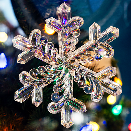 A close-up of a clear acrylic snowflake ornament. The snowflake has six delicate, branching arms and a smooth, reflective surface.