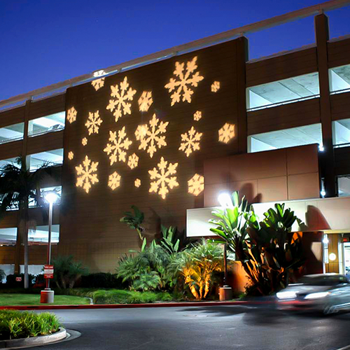 A projector displaying snowflakes on the side of a parking garage.