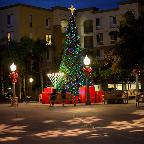 Projector displaying snowflakes on the ground in front of a Christmas tree.