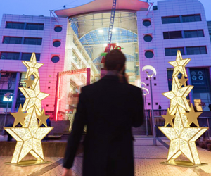 Man walking into a shopping center lined with two giant stacks of gold glitter stars lit with commercial Christmas lights
