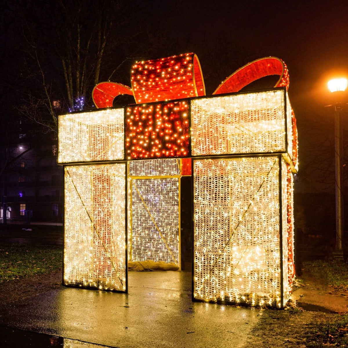 A walkthrough Christmas light display in the shape of a giant gift box. The box is decorated with red and warm white mini lights and is large enough for people to walk through.